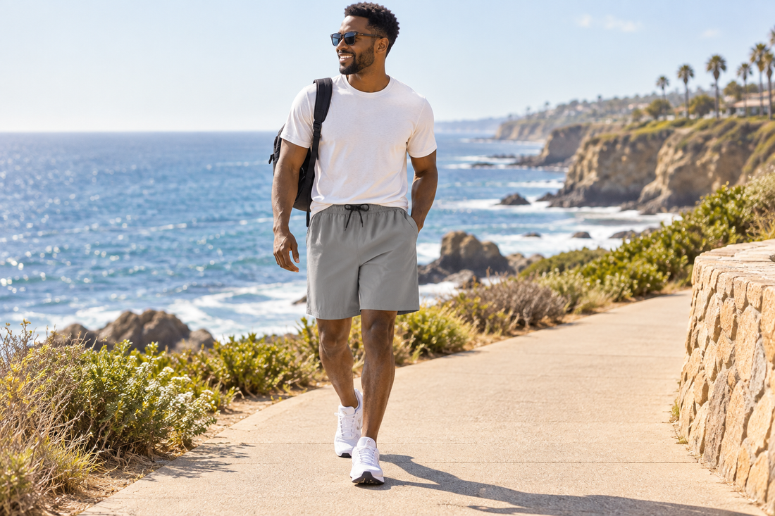 Man walking along a sunny coastal path in grey shorts, featured in a mens quick dry shorts size guide.