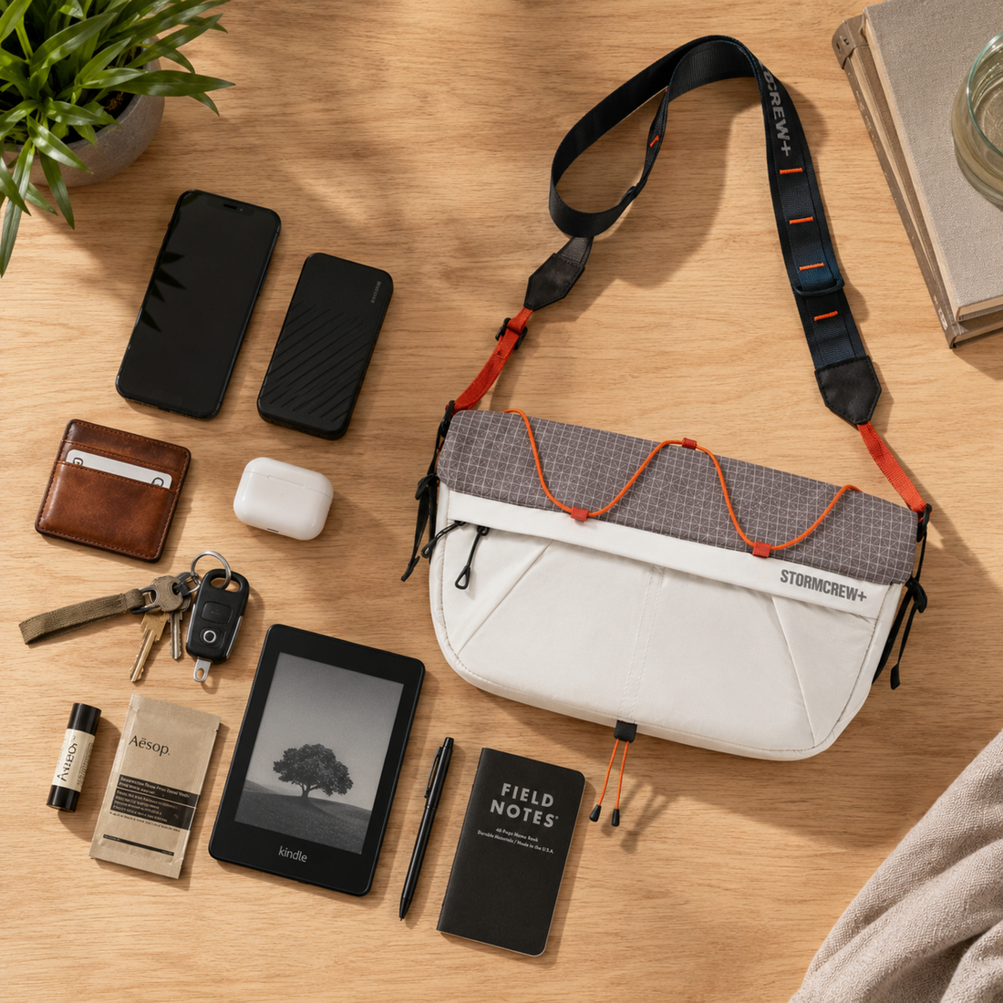 Flat lay of a phone, Kindle, and notebook showing what to carry in an everyday crossbody bag on a wooden table.